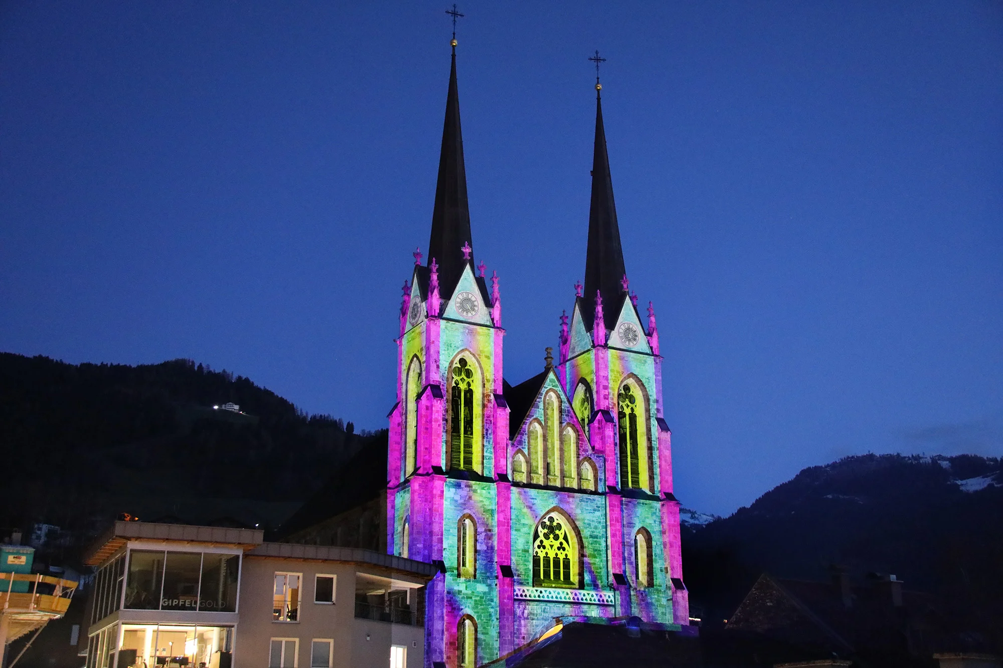 Grün-rosa Videomapping auf den zwei Türmen des Pongauer Doms in der Dämmerung