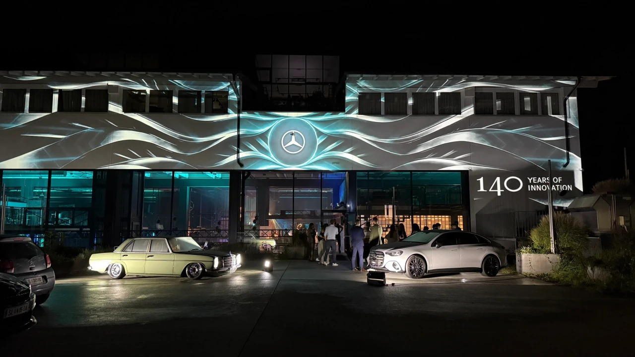 Türkis-weiße Wellen um den Mercedes-Stern auf der Fassade, mit Oldtimer und modernem Fahrzeug vor dem Eingang