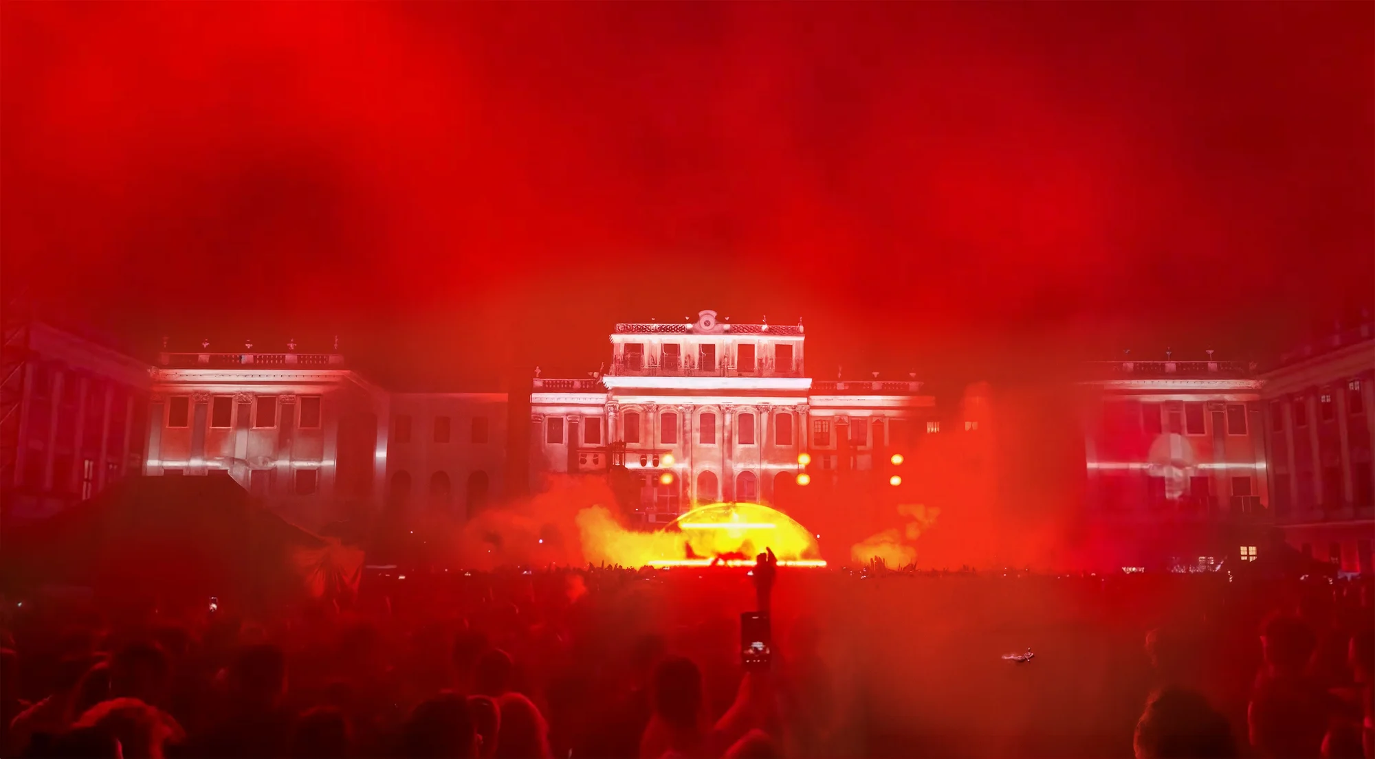 Red stage lighting and audience in front of the illuminated palace facade