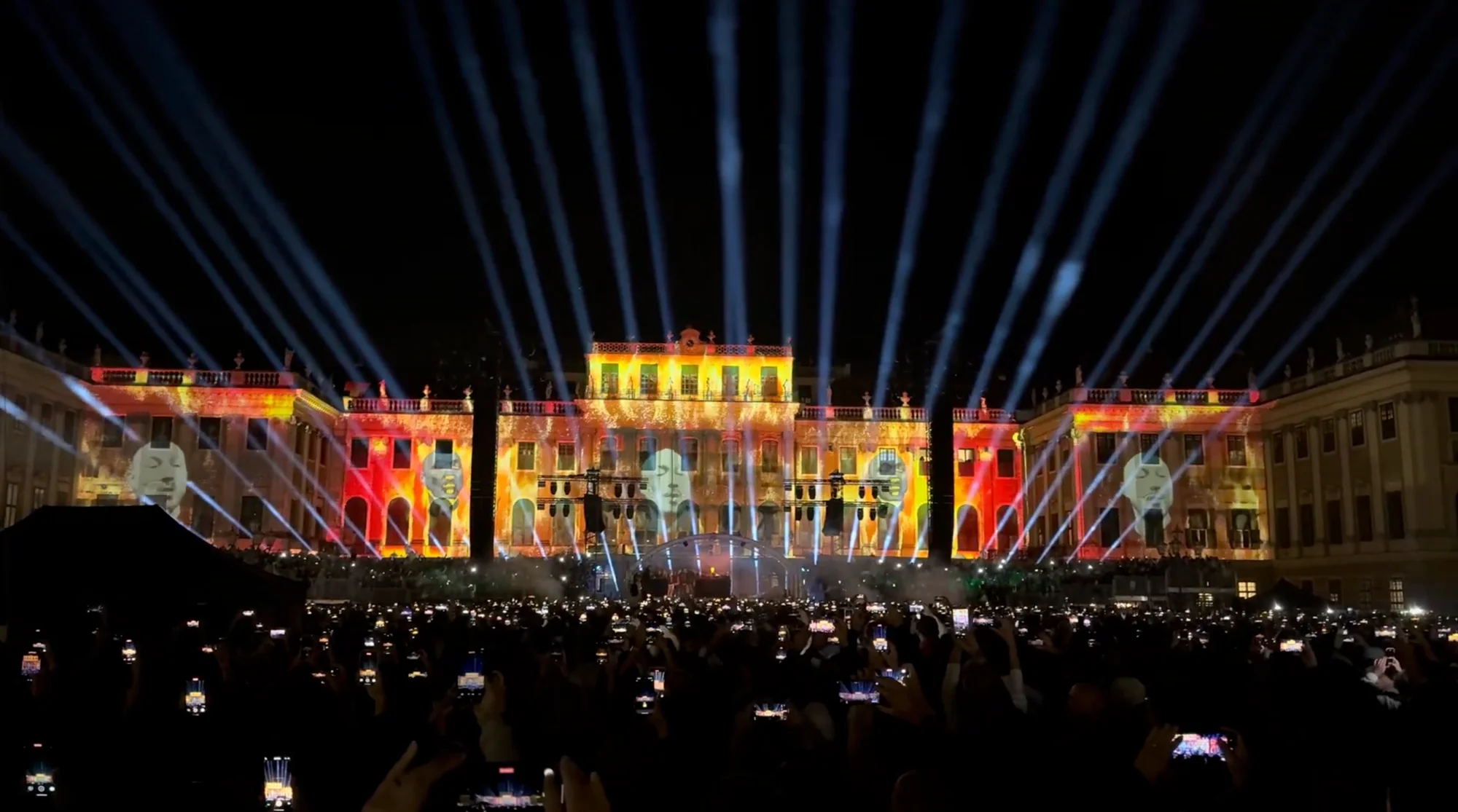 Concert audience in front of golden visuals and light beams at Schönbrunn Palace