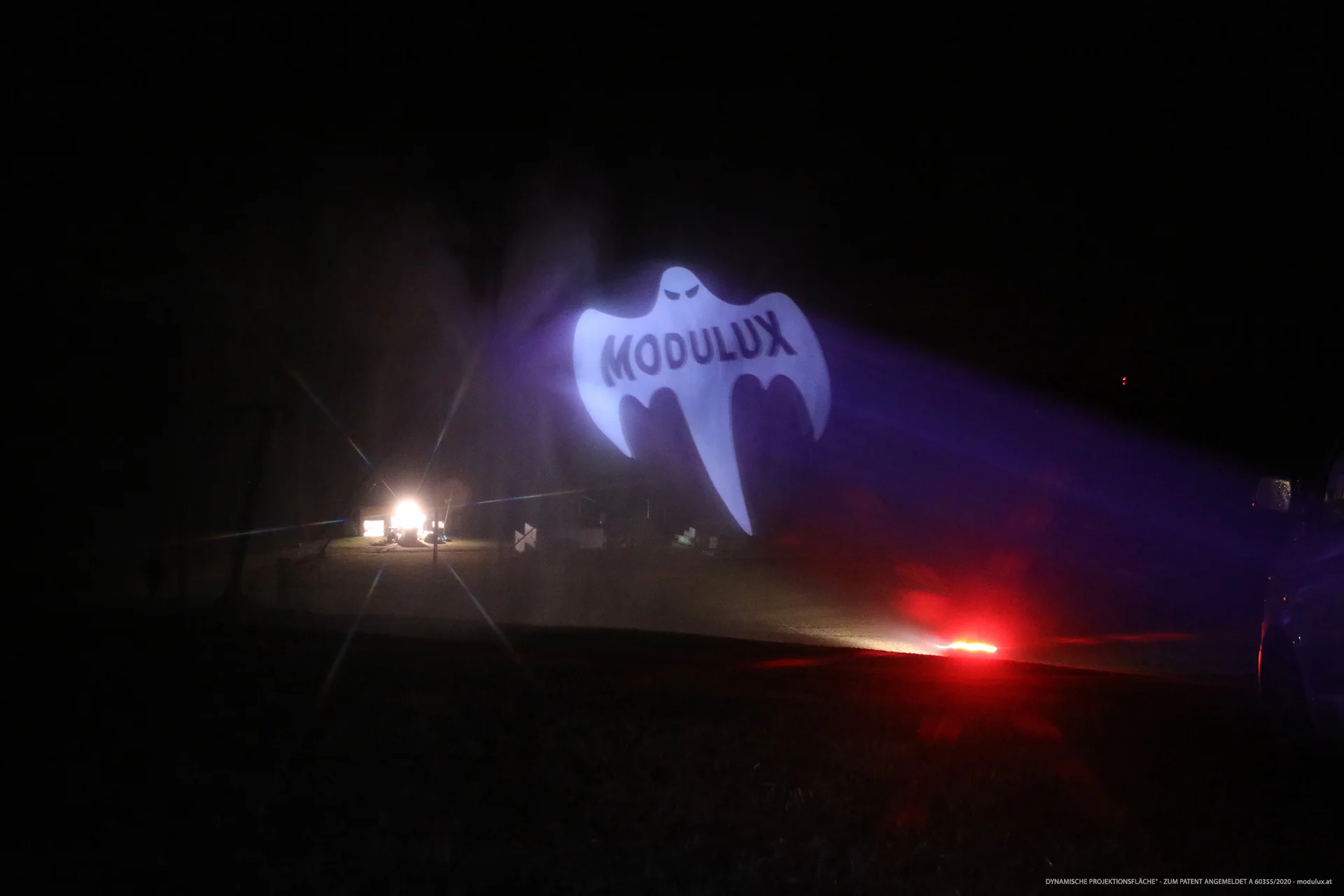 Wide night view of the MODULUX ghost projection with red and white lights